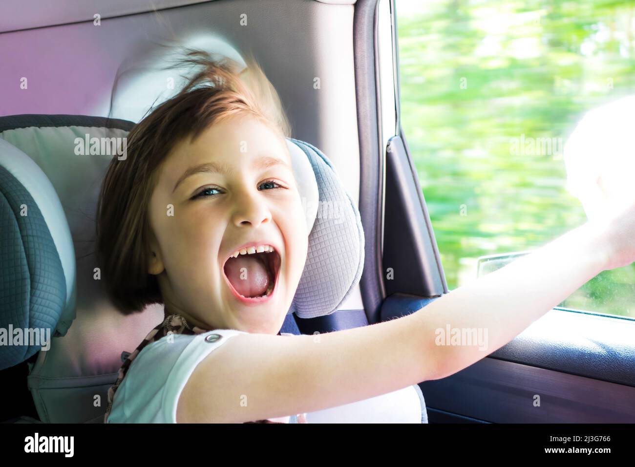 Little happy girl  in a car near the open window. Kid on a road trip. Shallow depth of field. Stock Photo