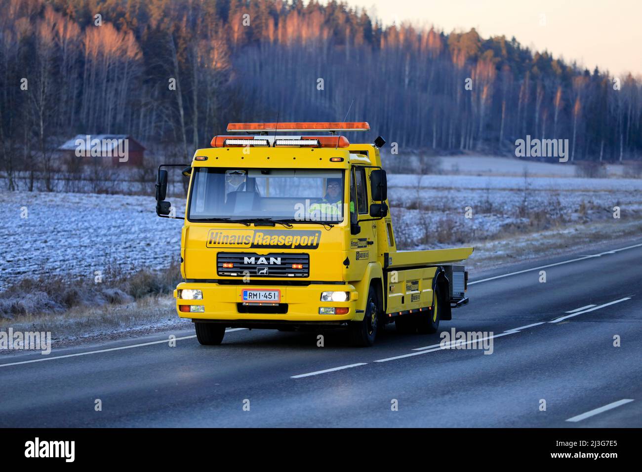 Yellow MAN flatbed tow truck of Hinaus Raasepori at speed on highway 52 near sunset time in winter. Salo, Finland. December 22, 2021. Stock Photo