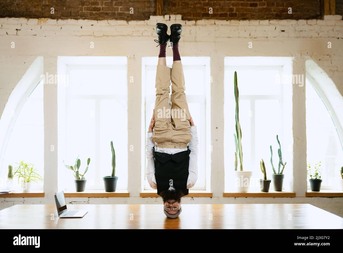 Office clerk having fun, doing headstand without hands on wooden table