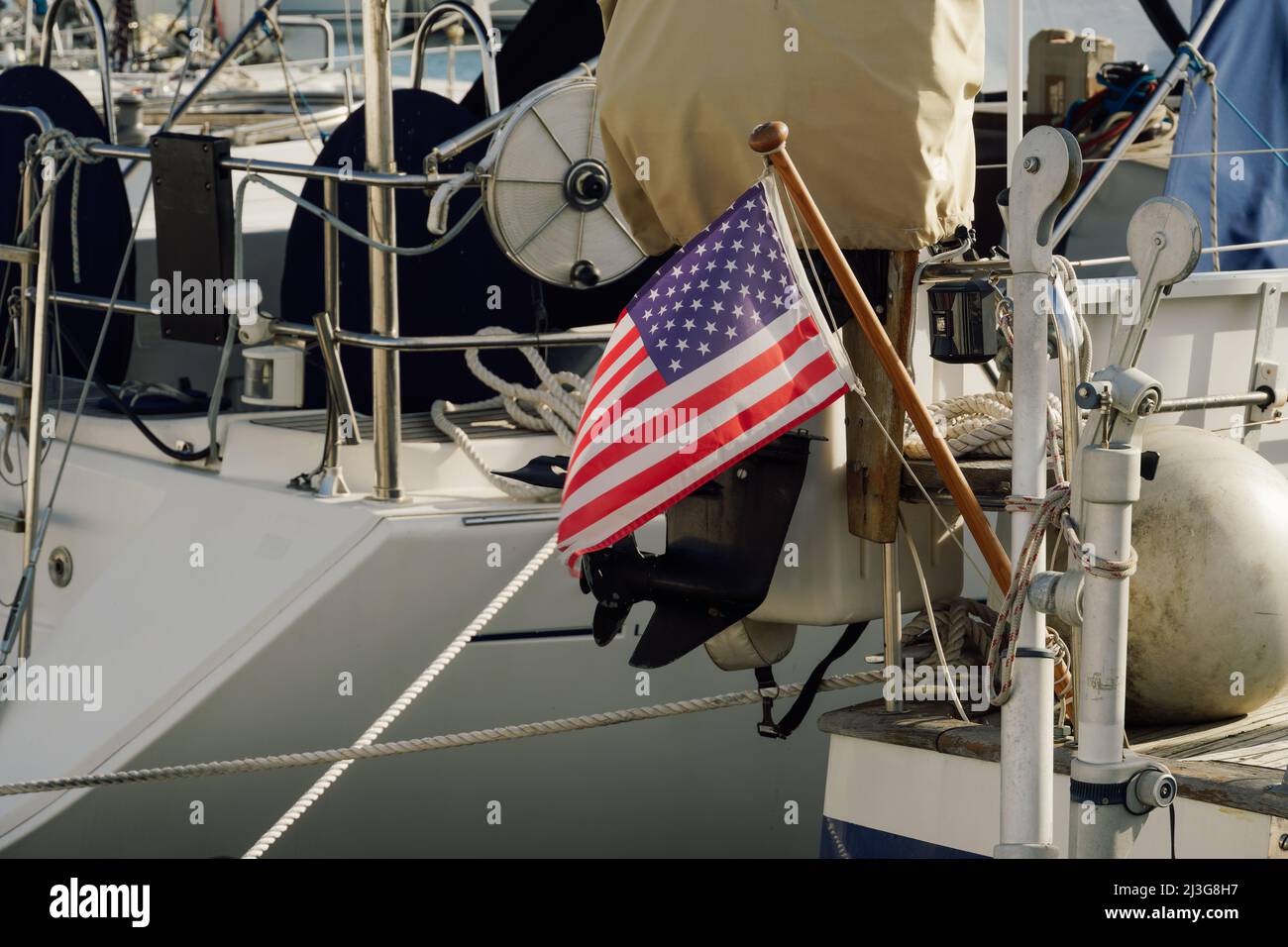 United States American national flag with stars and stripes on a wooden mast waving against the wind on the back of a moored boat at a marina. Stock Photo