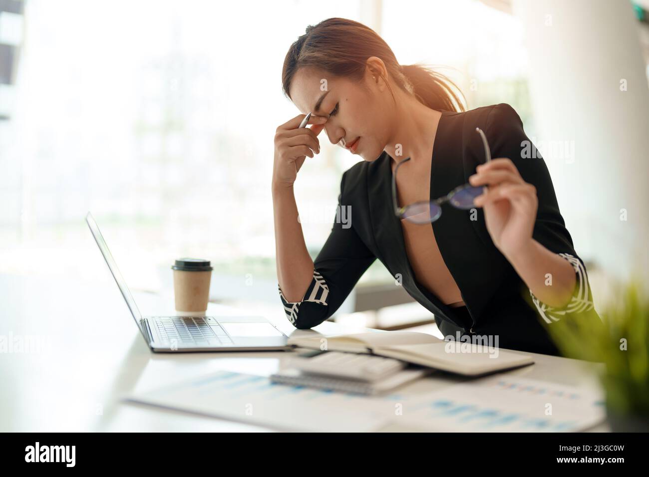 Very stressed business asian woman sitting in front of her computer looking at a large pile of paperwork, while holding a hand at her forehead Stock Photo