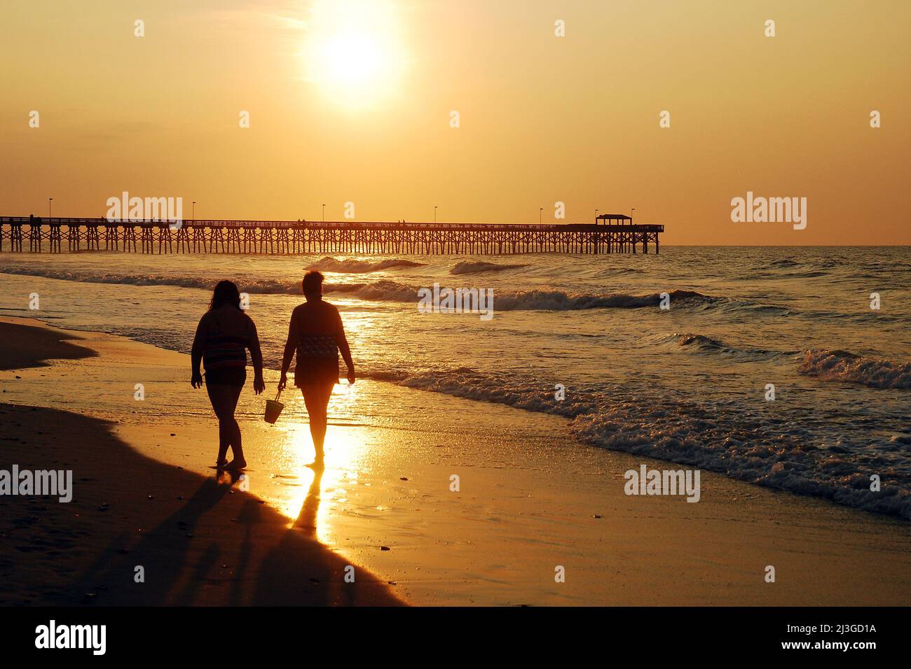 Two women enjoy a sunrise stroll along the shore in Myrtle Beach, South Carolina Stock Photo