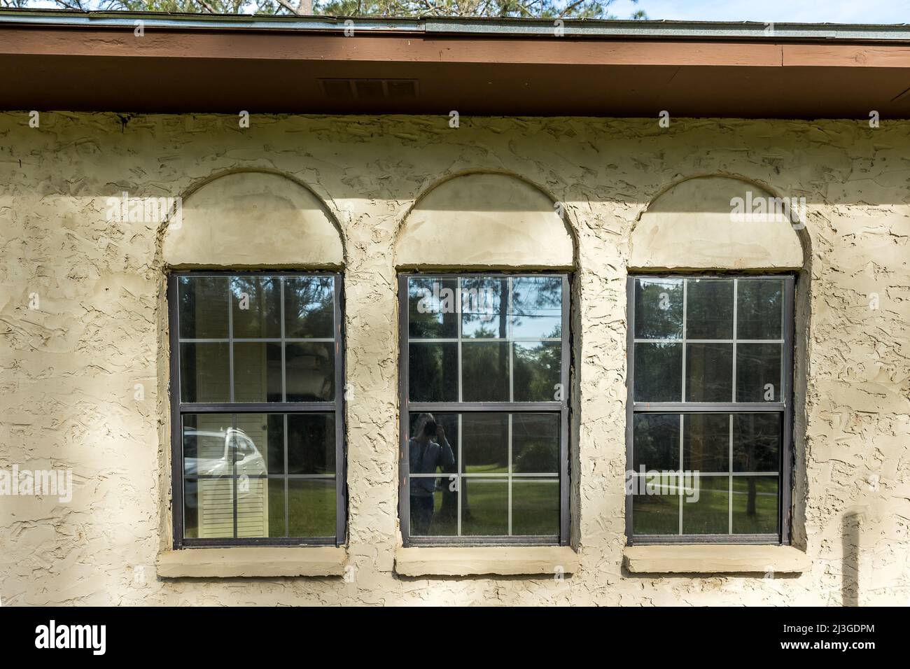 The side view of a brown 1970's ranch style spanish style villa stucco cinder block home with architectural arches and black aluminium original Stock Photo