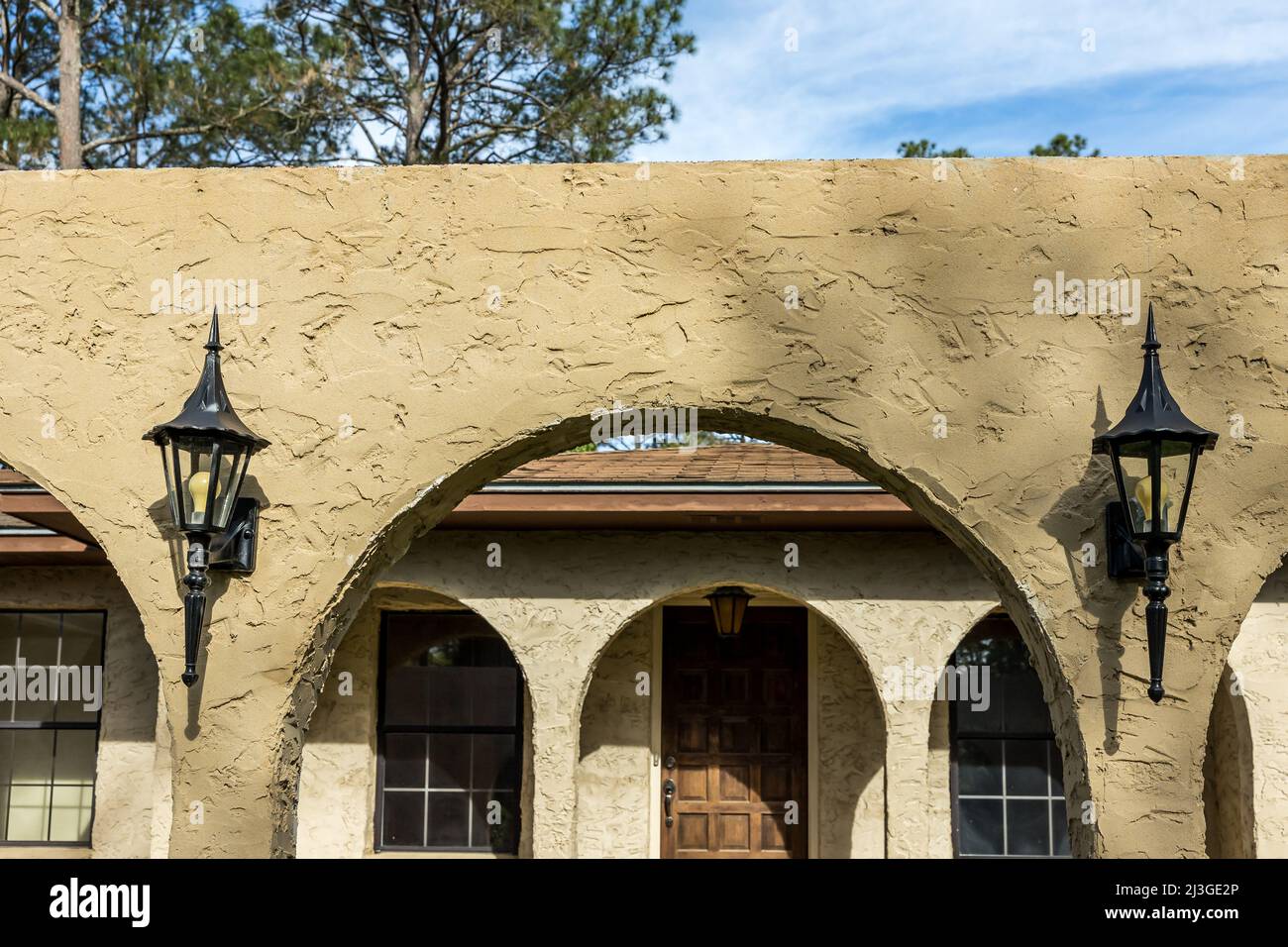 The top front view of a brown 1970's ranch style spanish style villa stucco cinder block home with architectural arches and black aluminium original Stock Photo