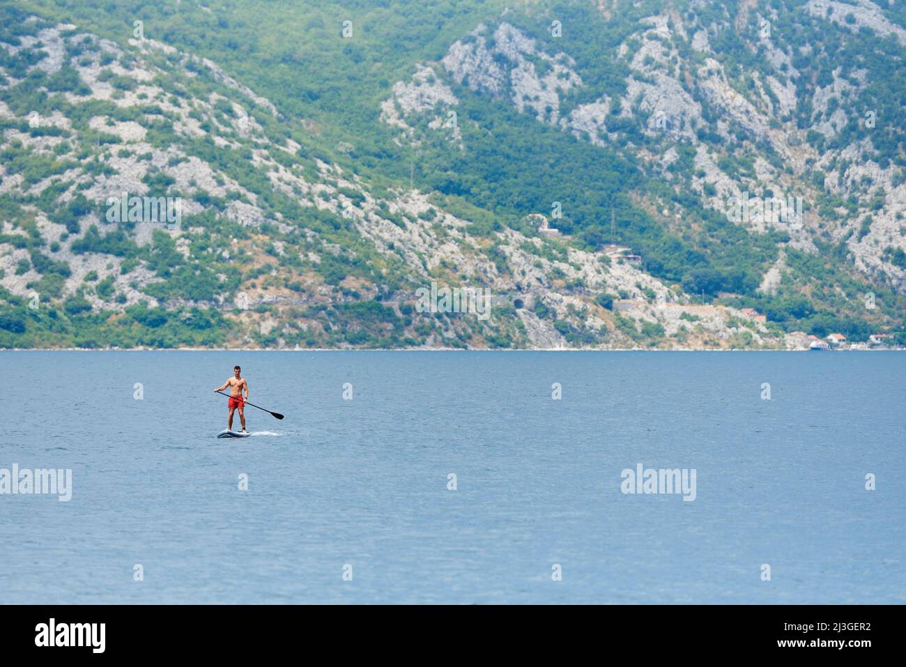 PERAST, MONTENEGRO - JULY 20, 2021: Young man rides on a paddle board in the sea Stock Photo