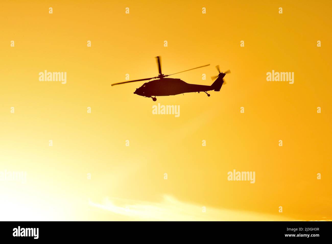 Silhouette of military Sikorsky Black Hawk UH-60 helicopter in flight and flying over Pacific Ocean at golden sunset, San Diego, California, USA Stock Photo