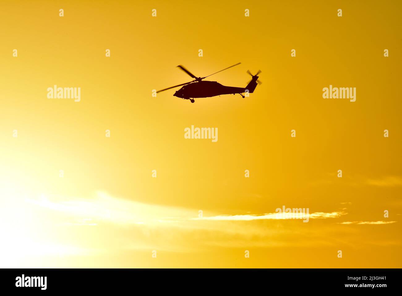 Silhouette of military Sikorsky Black Hawk UH-60 helicopter in flight and flying over Pacific Ocean at golden sunset, San Diego, California, USA Stock Photo