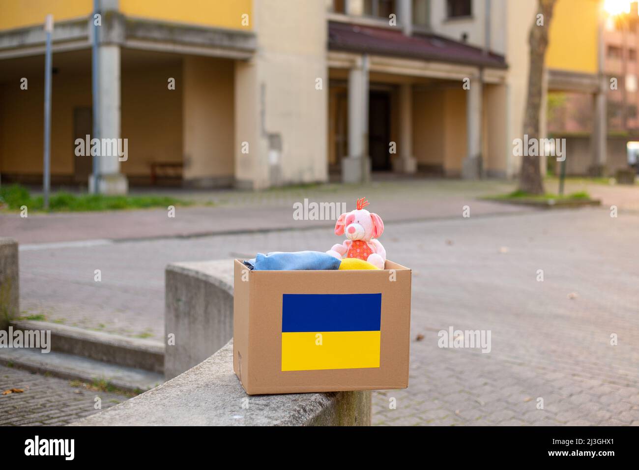 A box with a Ukrainian flag for donating humanitarian aid with things and children's toys for Ukrainian refugees on the street. Stay with Ukraine.  Stock Photo