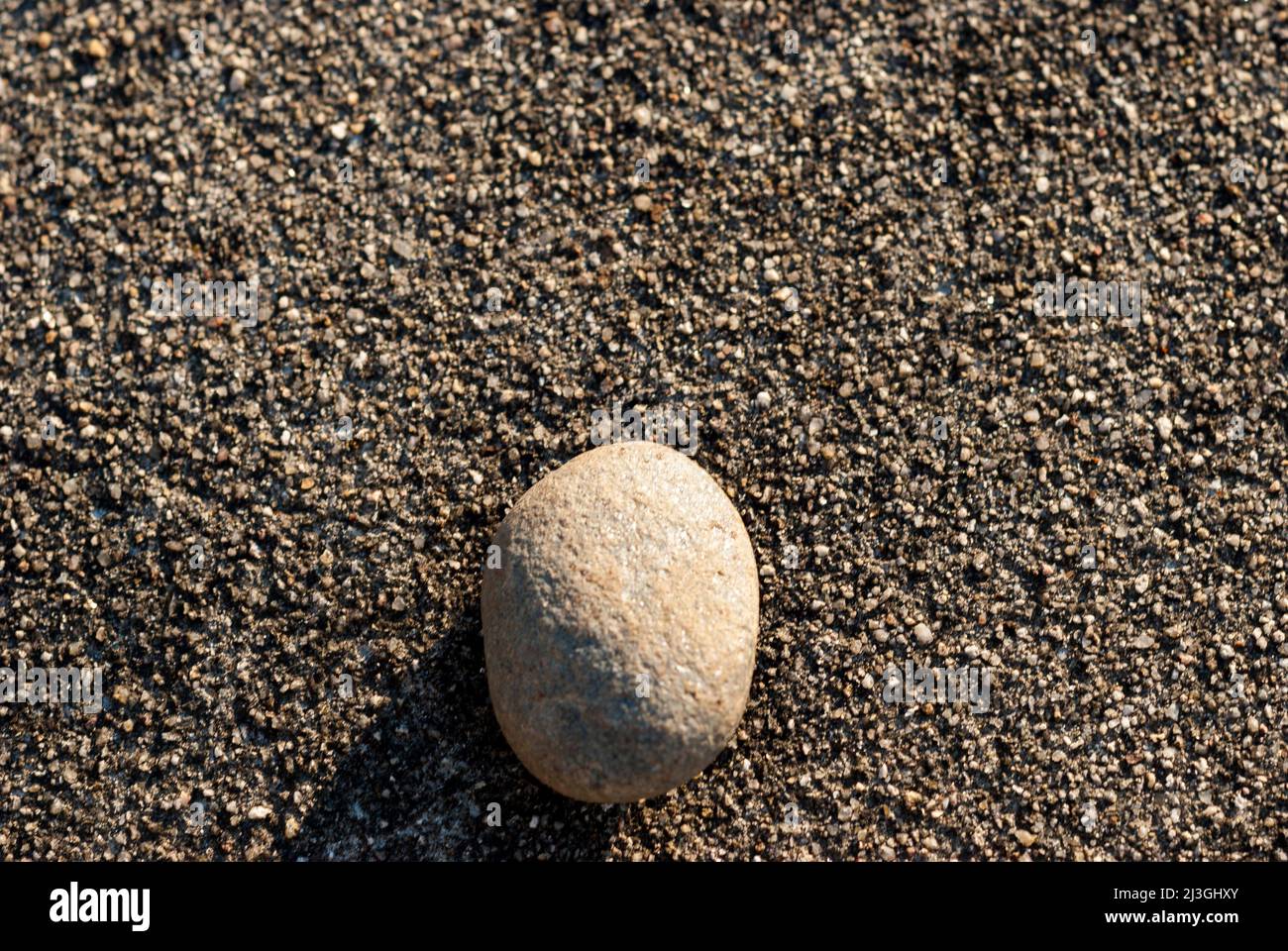 Small white stone isolated on dark gravel background in horizontal with sun Stock Photo