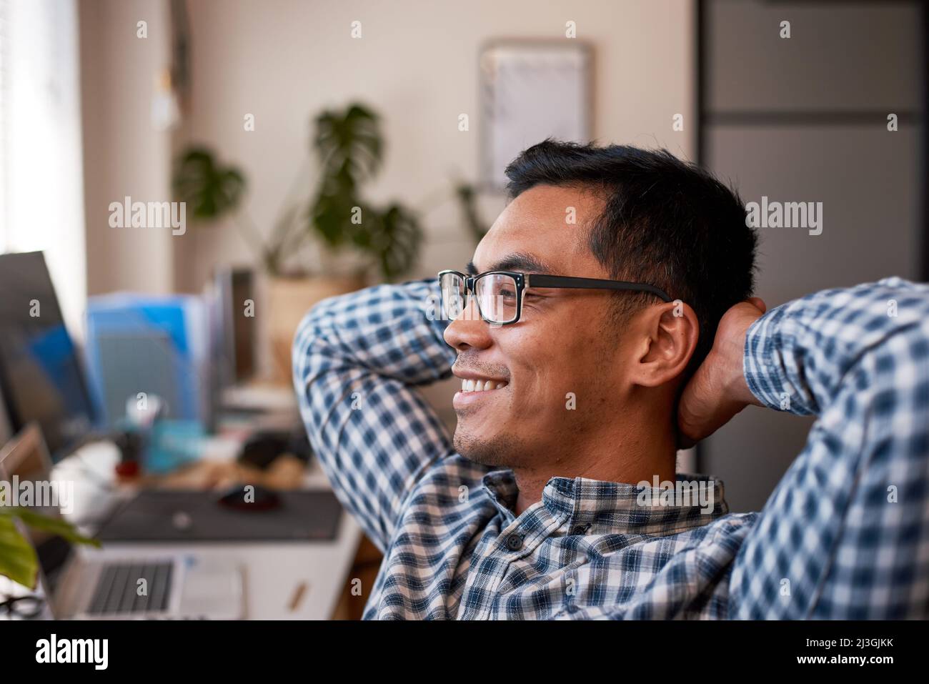 A young office worker leans back relaxing in his desk wearing spectacles Stock Photo