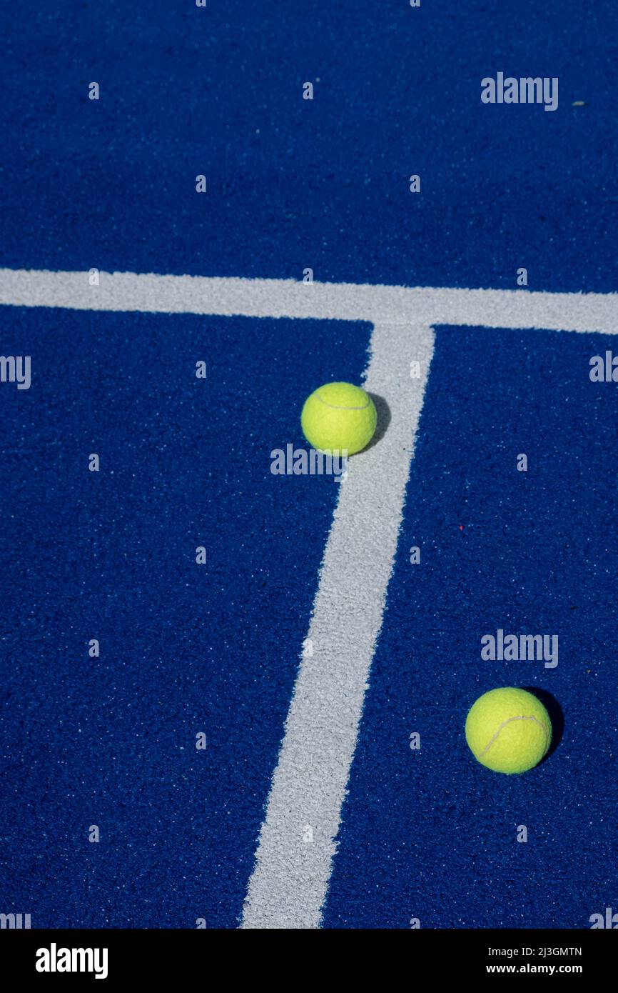 two paddle tennis balls next to the lines of a blue paddle tennis court