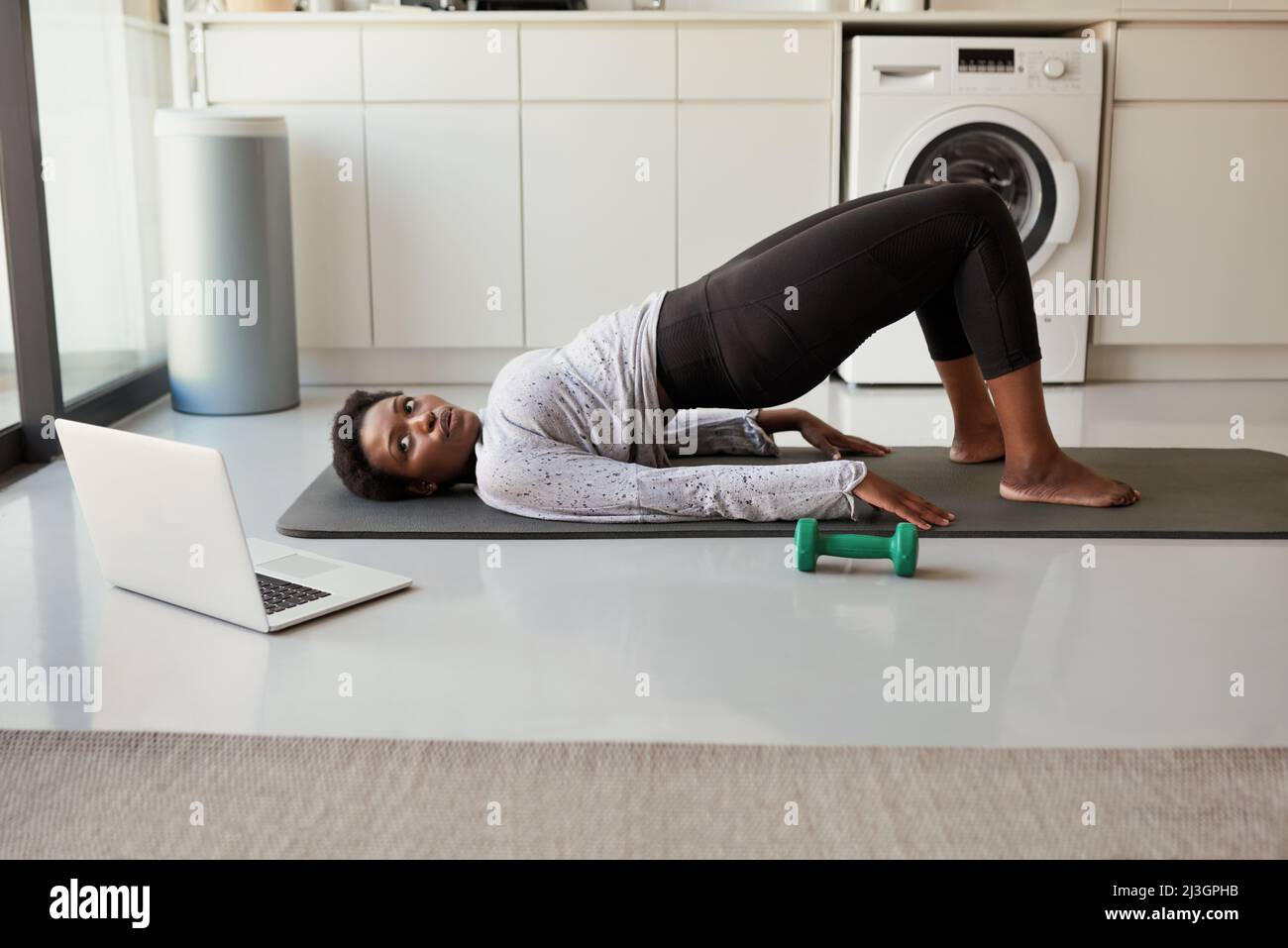 Becoming fit all in the privacy of her home. Shot of a young woman using a laptop while exercising at home. Stock Photo