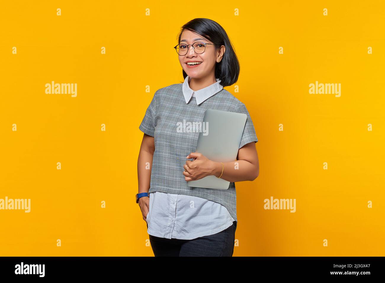 Portrait of cheerful Asian woman wearing glasses carrying laptop and ...