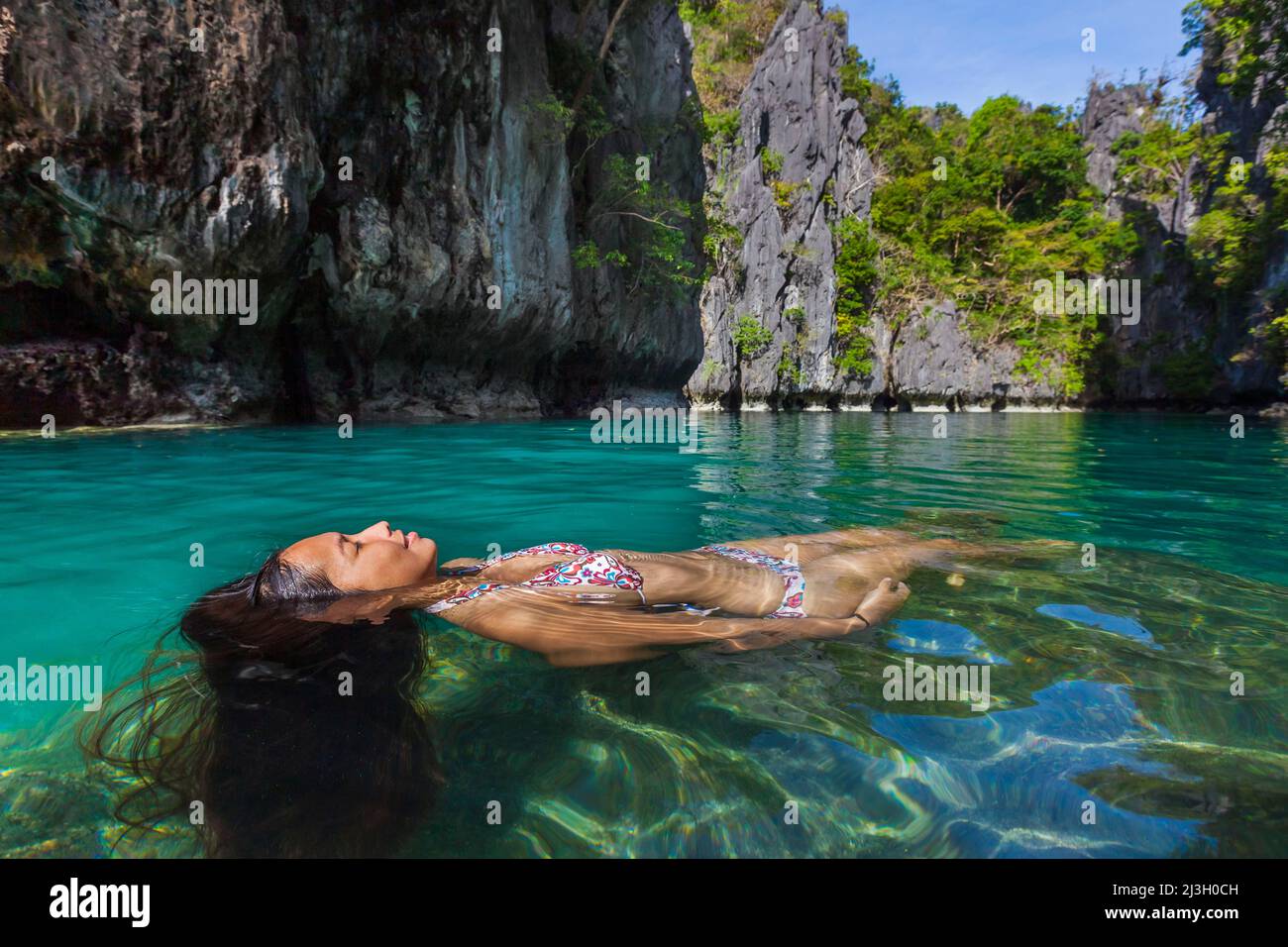 Philippines, Palawan, El Nido, Bacuit Archipelago, Miniloc Island, Small Lagoon, a young Filipina woman wearing a bikini re-enacts John Everett Millais' painting, Ophelia, in turquoise water and tropical environment, surrounded by karst cliffs Stock Photo