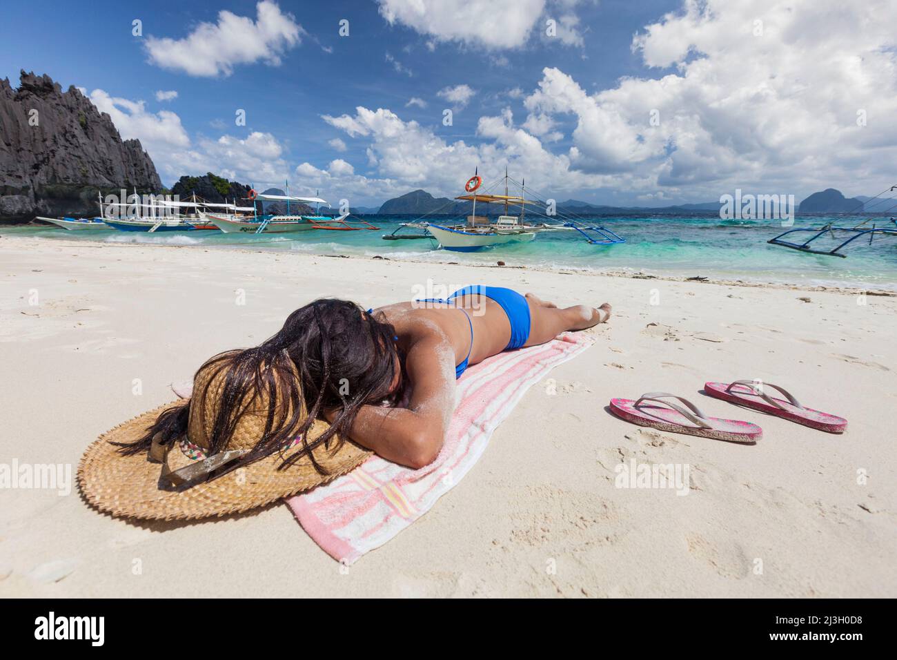 Philippines, Palawan, El Nido, Bacuit Archipelago, Shimizu Island, young Filipino woman in blue bikini with a straw hat, lying on the white sand beach Stock Photo