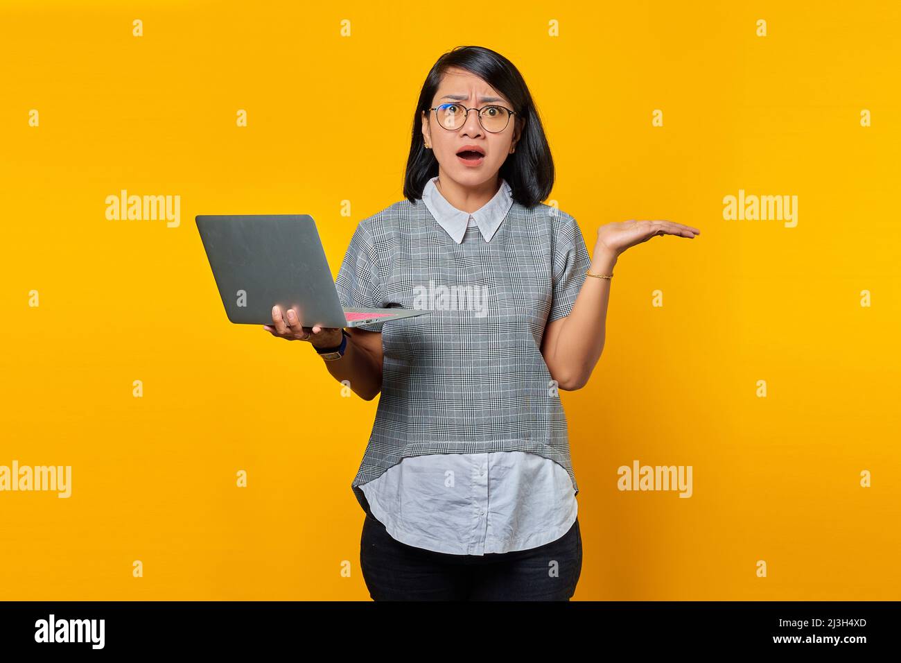 Portrait of Asian woman wearing glasses in surprise holding laptop with ...