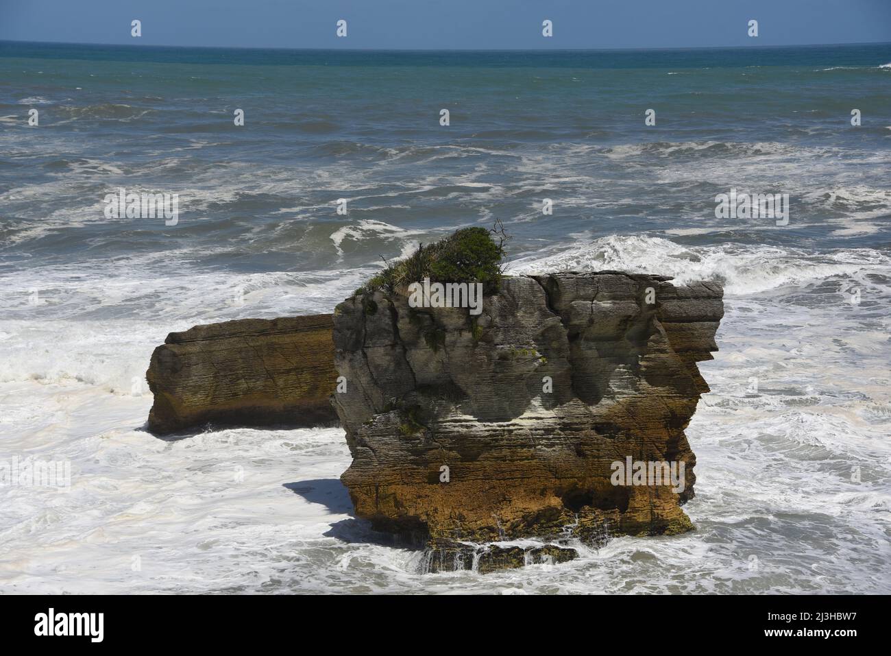A panoramic view of the foamy ocean, surf and sea stacks just off the beach at the popular Punakaiki Pancake Rocks on the South island of New Zealand. Stock Photo