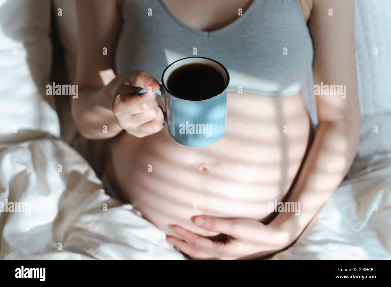 A pregnant woman holds a cup of coffee in her hands. Caffeine safety