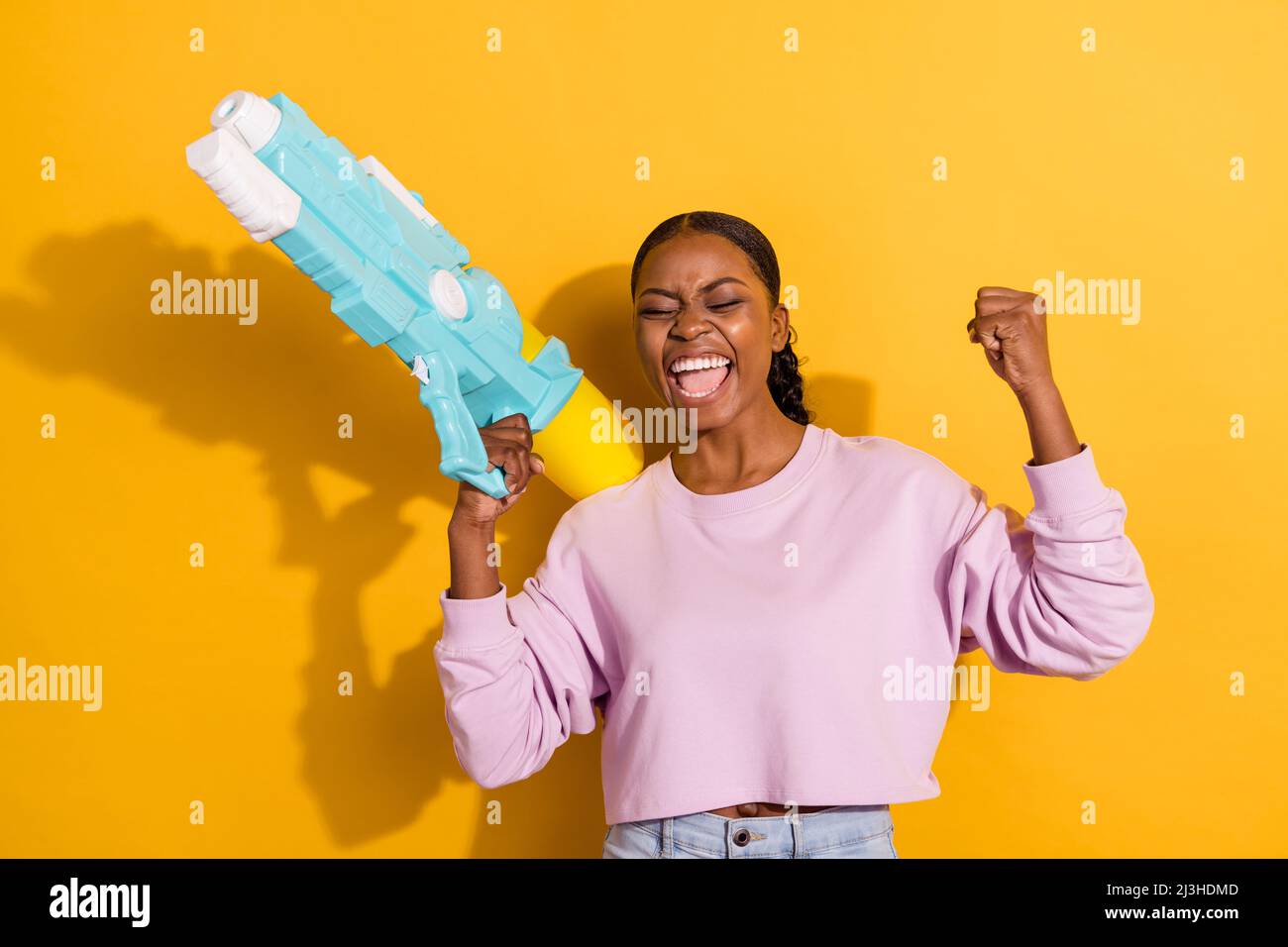 Portrait of delighted carefree person raise fist scream yeah hold water pistol isolated on yellow color background Stock Photo