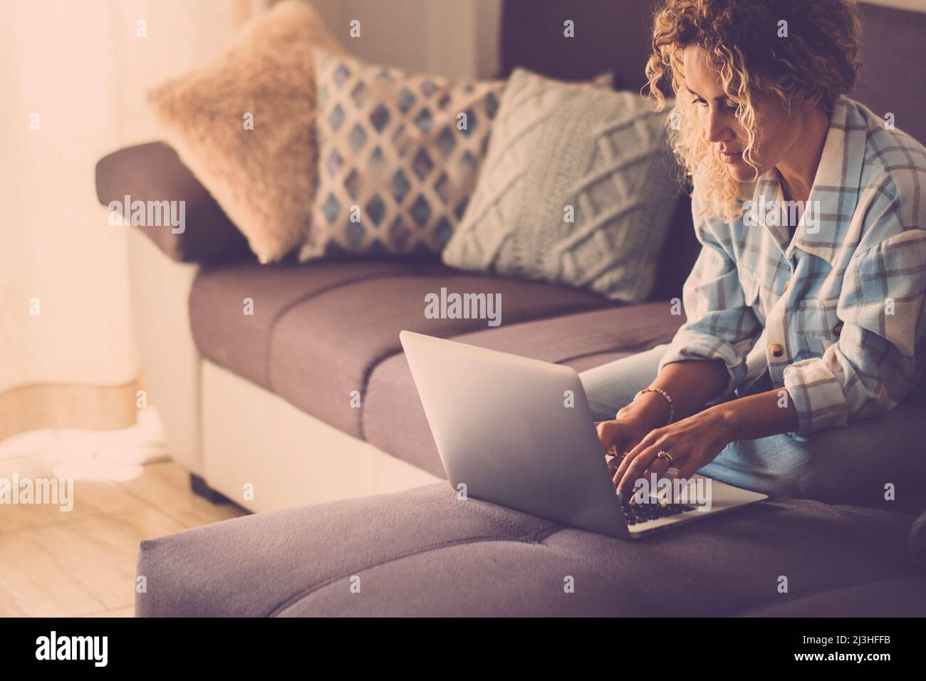Modern woman working online with laptop computer comfortably sitting on the sofa at home. Stock Photo