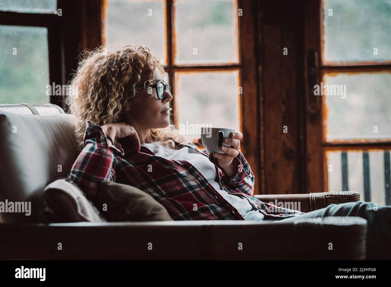 woman, blonde, curls, check shirt, armchair, cozy, sit, side, cup, hold Stock Photo