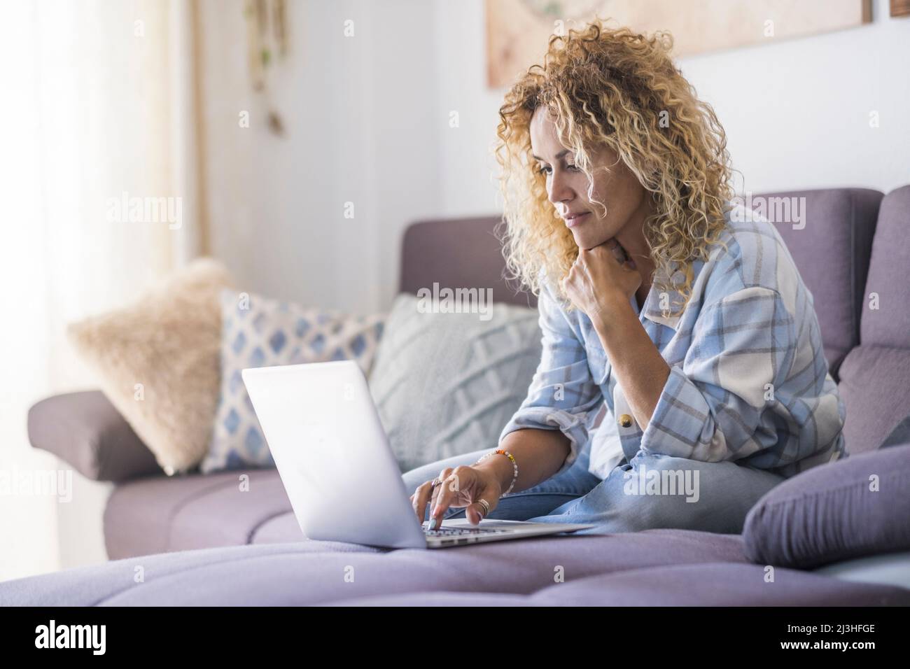 Modern woman working online with laptop computer comfortably sitting on the sofa at home. Stock Photo