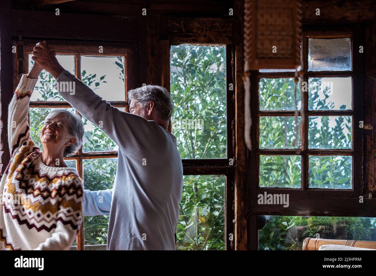 Elderly people happy lifesryle activity with two senior man and woman dancing excited at home for love and relationship - Mature couple have fun at the chalet during holiday vacation or mountains house life Stock Photo