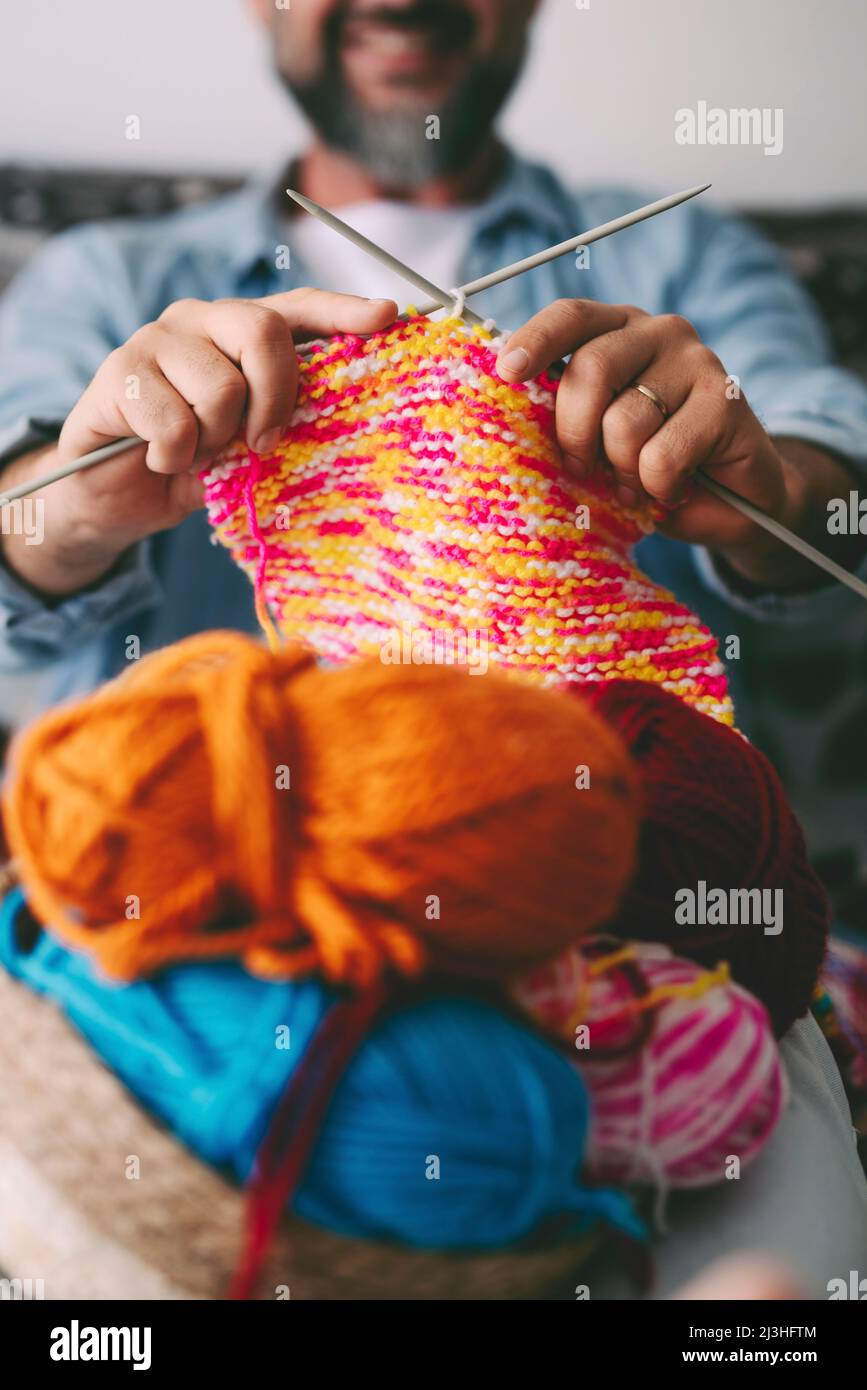 Close up of adult man working with ball yarn of colorful wool. Happy people in indor hobbies activity using woolen and doing knitting work. Indoor leisure activity Stock Photo