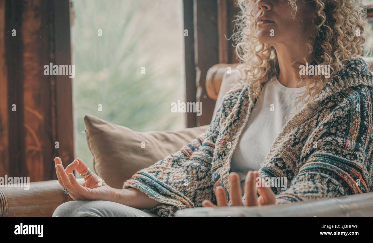 Close up of adult woman in yoga position and meditation indoor activity at home - concept of healhty and relaxed lifestyle people - female sitting and enjoying peace and mindfulness exercise Stock Photo
