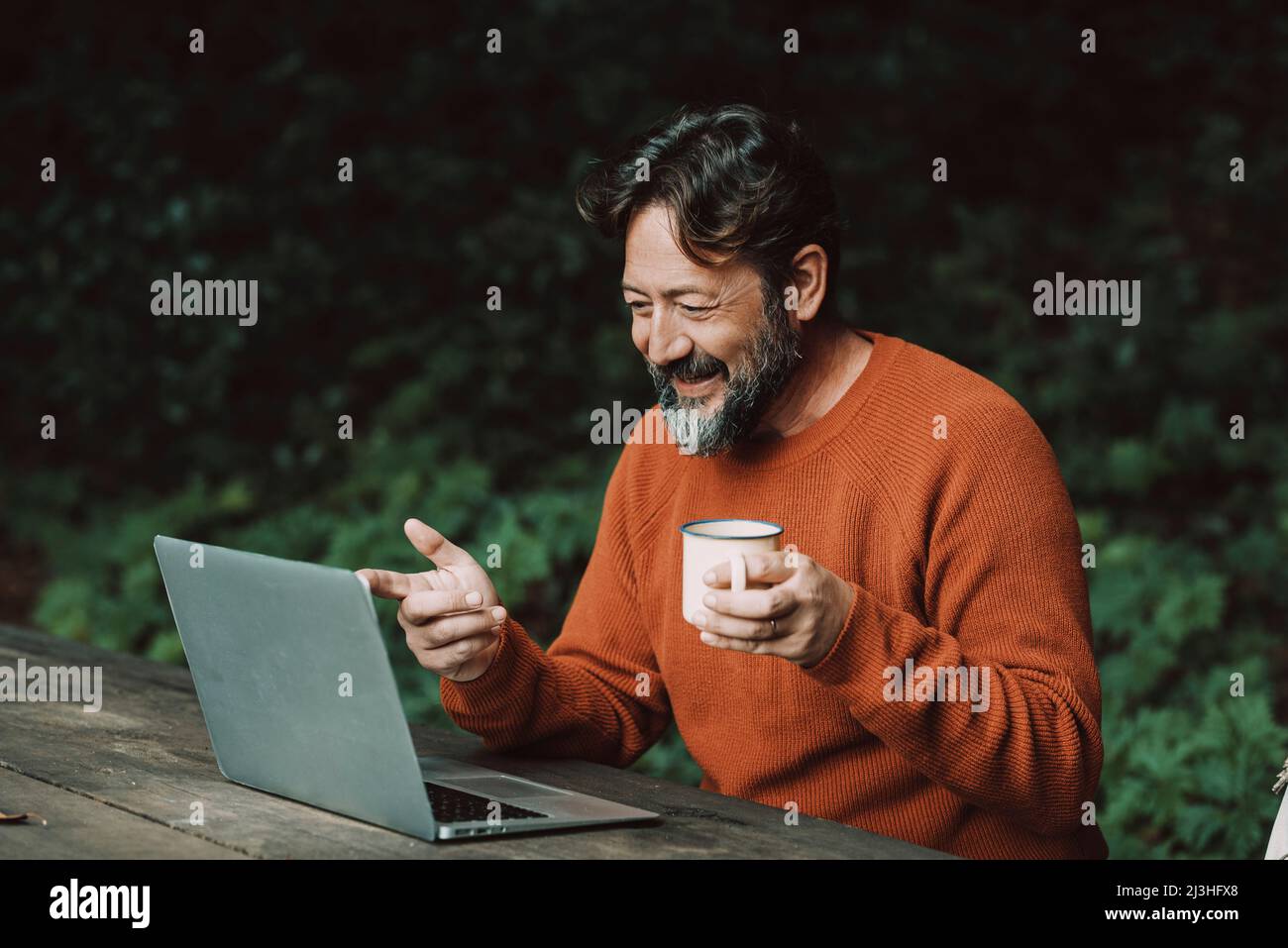 Adult hipster bearded man enjoying video call conference outdoors in the nature using laptop computer. Concept of modern people and digital nomad smart working job activity outdoors Stock Photo