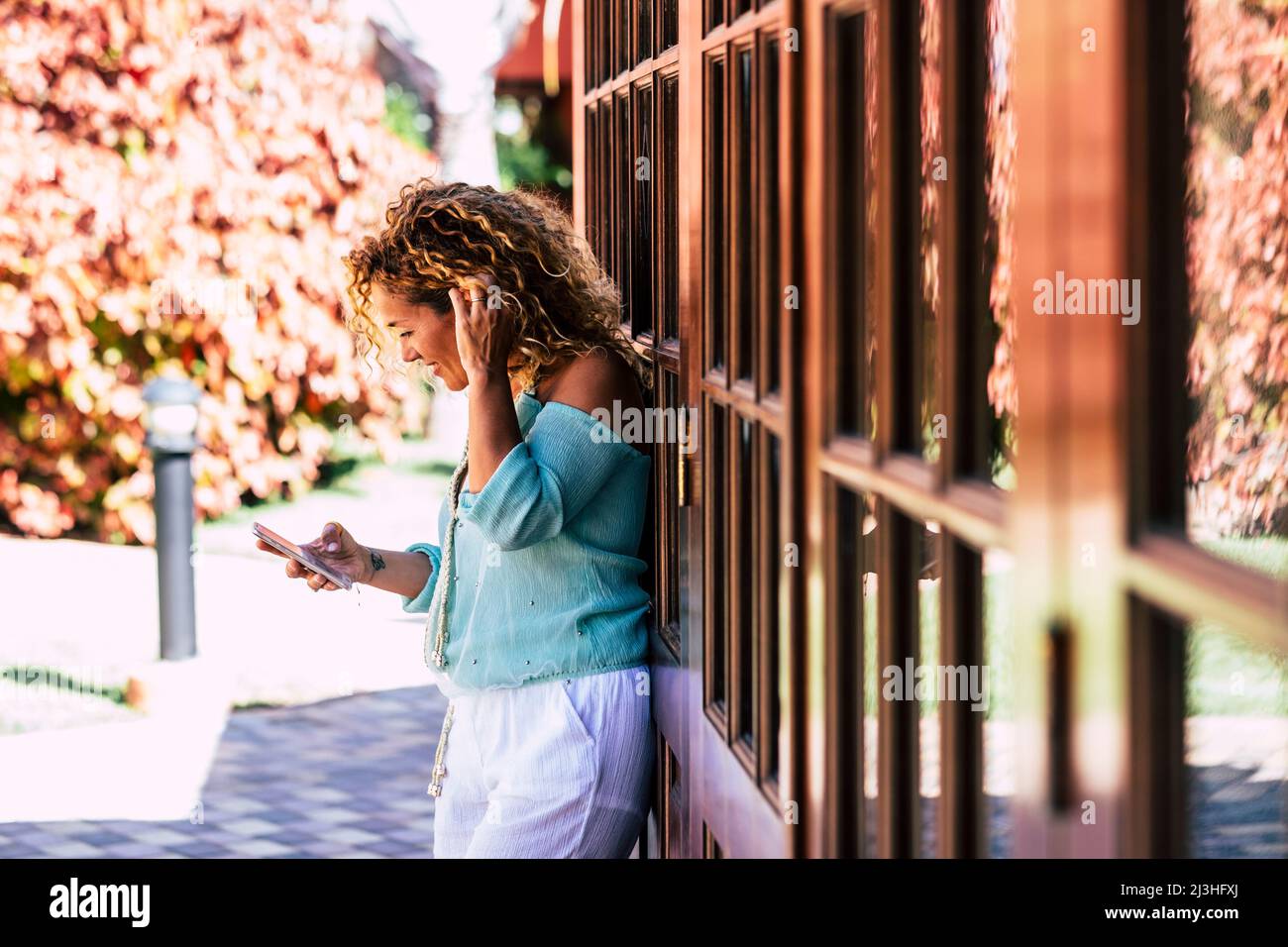 Woman with smartphone in front of her house, happy, smile Stock Photo