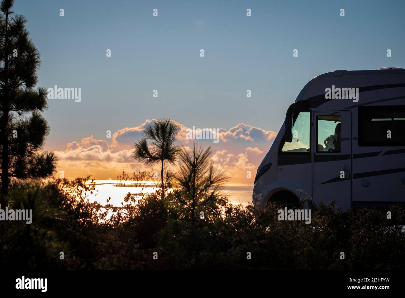 Travel people lifestyle and nomadic life with white camper van motorhome and beautiful colorful sunset on the ocean in background. Travel and enjoy freedom and nature with rv Stock Photo