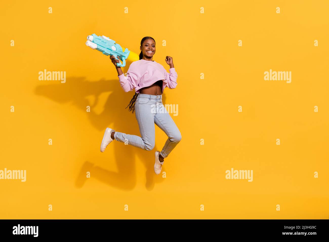 Full body portrait of carefree energetic girl raise fist hold water pistol isolated on yellow color background Stock Photo