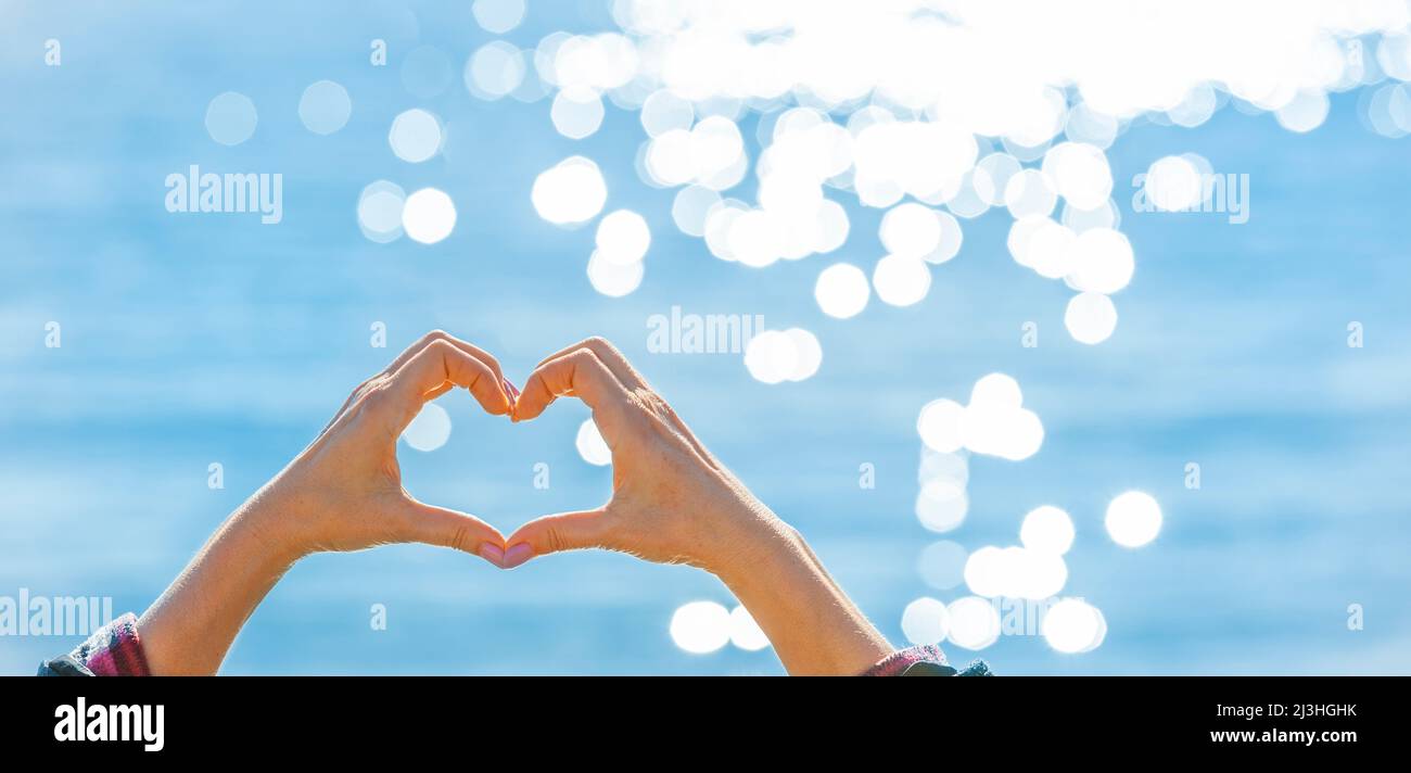 A hand forms a heart in front of glittering water Stock Photo