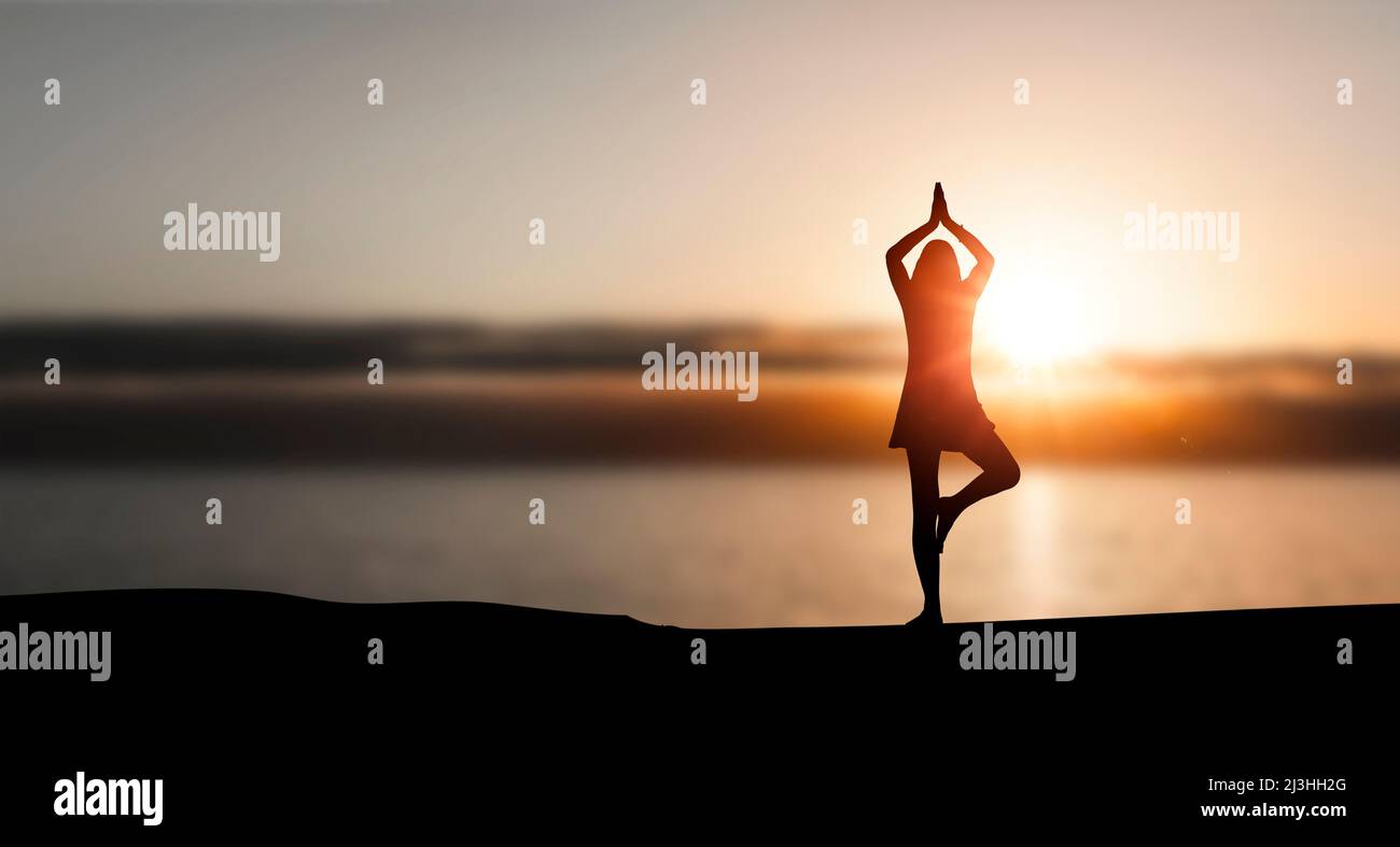 Silhouette of woman doing yoga on beach Stock Photo
