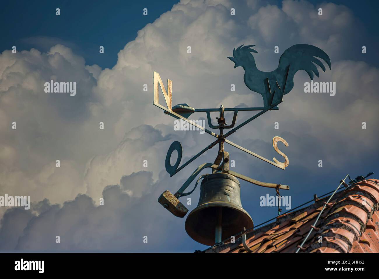 A weathercock on the roof with cardinal direction indicator and a striking hammer for a bell Stock Photo