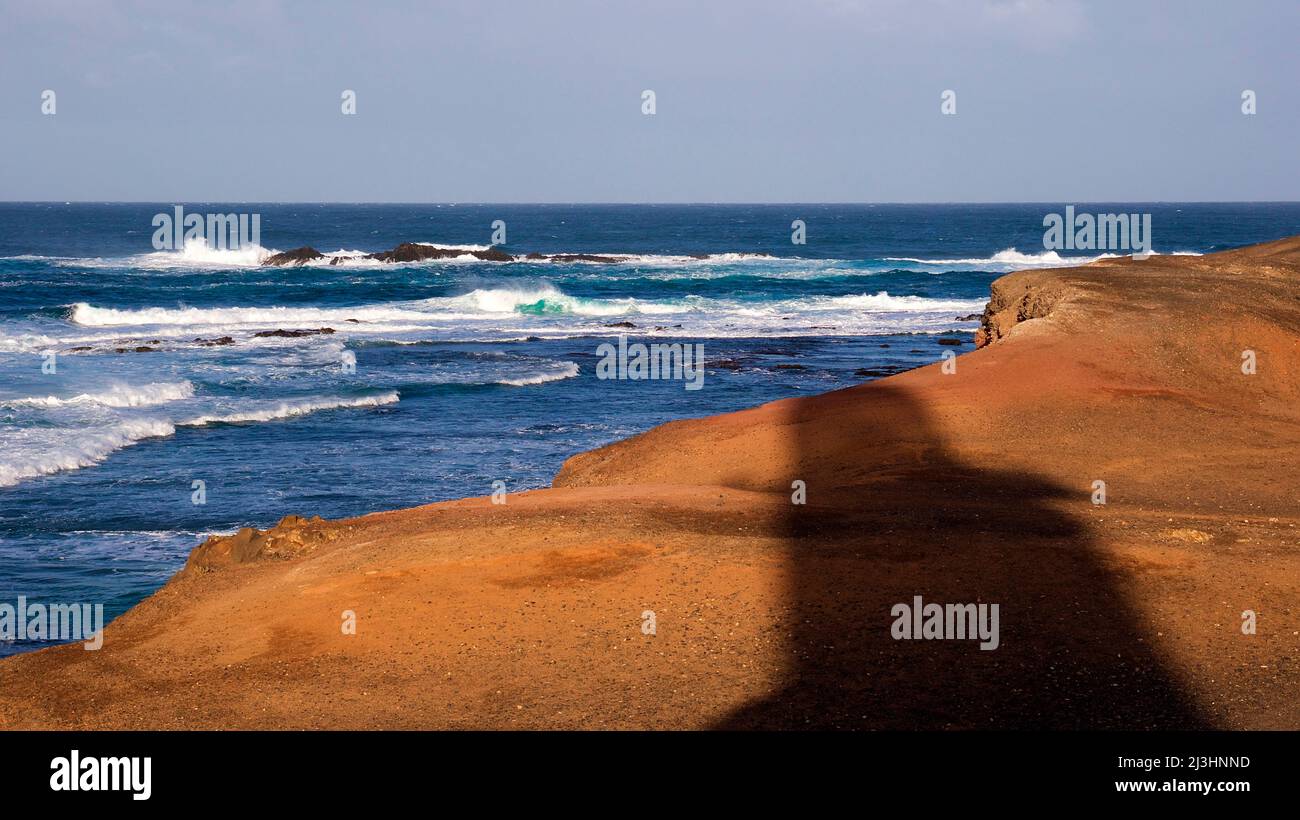 Spain, Canary Islands, Fuerteventura, southwest tip, barren landscape, Punta de Jandia, red mainland coast, waves, surf, shadow of lighthouse Stock Photo