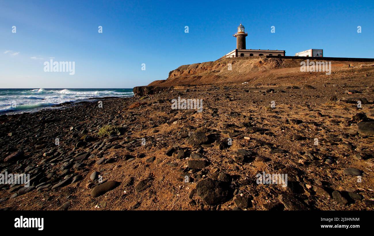 Spain, Canary Islands, Fuerteventura, southwest tip, barren landscape, Punta de Jandia, lighthouse, wide angle shot, in the foreground beach with pebbles, left sea, sky blue Stock Photo