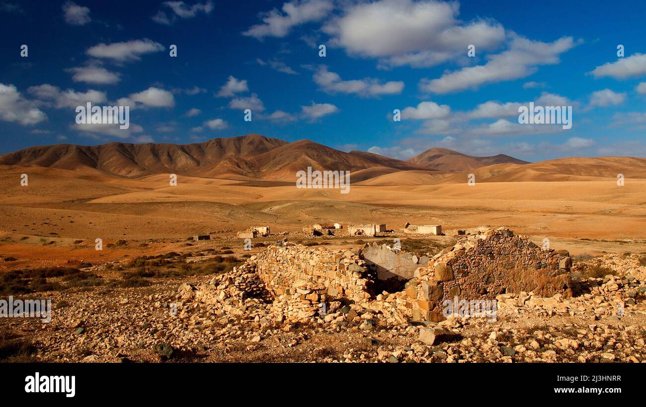 Spain, Canary Islands, Fuerteventura, island interior, barren landscape, dry. desert-like, barren mountain range, blue sky with white clouds, ruined building in the foreground, isolated abandoned buildings in the middle ground Stock Photo