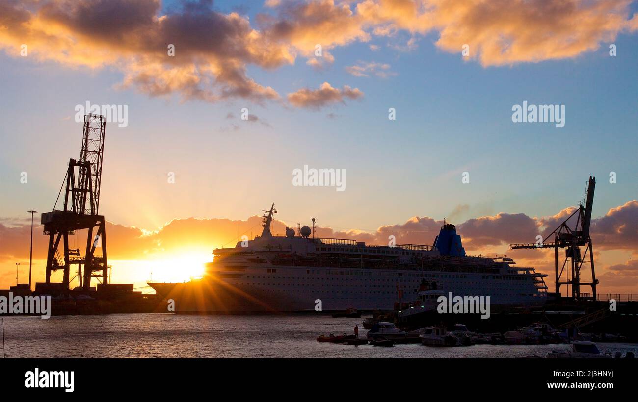 Spain, Canary Islands, Fuerteventura, capital, Puerto del Rosario, backlight, sunrise, left loading crane as silhouette, in the middle cruise ship, right loading crane as silhouette, sky light blue, clouds gray illuminated by morning sun Stock Photo