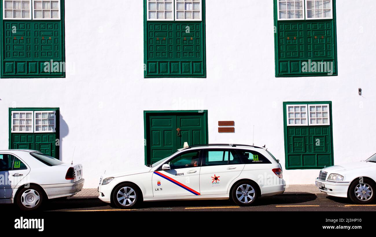 Canary Islands, Lanzarote, volcanic island, capital Arrecife, building white with green doors and windows, cars parked in front, the middle one is a cab Stock Photo