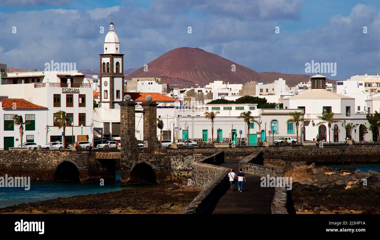Canary Islands, Lanzarote, volcanic island, capital Arrecife, view from the bridge Puente de las Bolas to Arrecife and church Parroquia de San Ginés, in the background a reddish lava hill can be seen, sky blue with many grey-white clouds Stock Photo