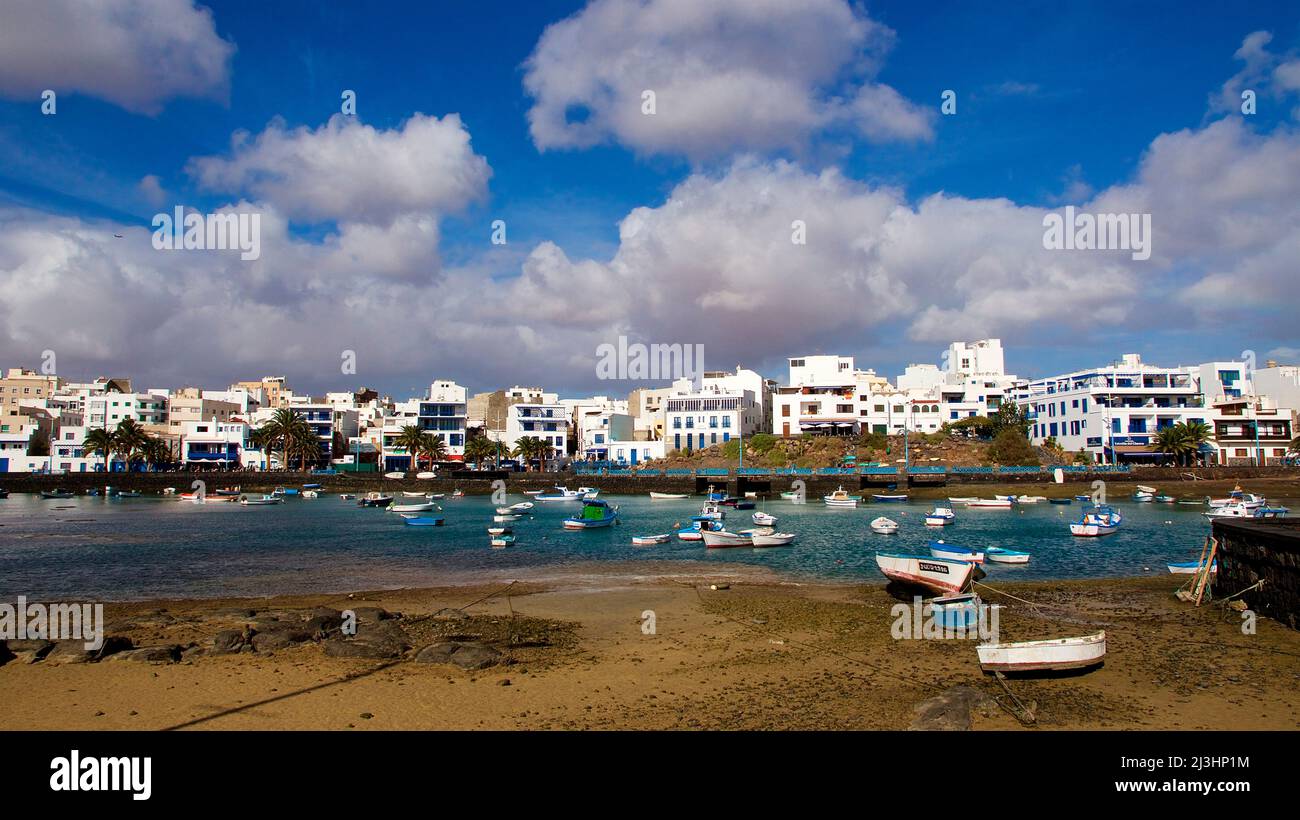 Canary Islands, Lanzarote, volcanic island, capital Arrecife, view over beach and harbor to part of Arrecife, boats in water, boats on land, sky blue, clouds white Stock Photo