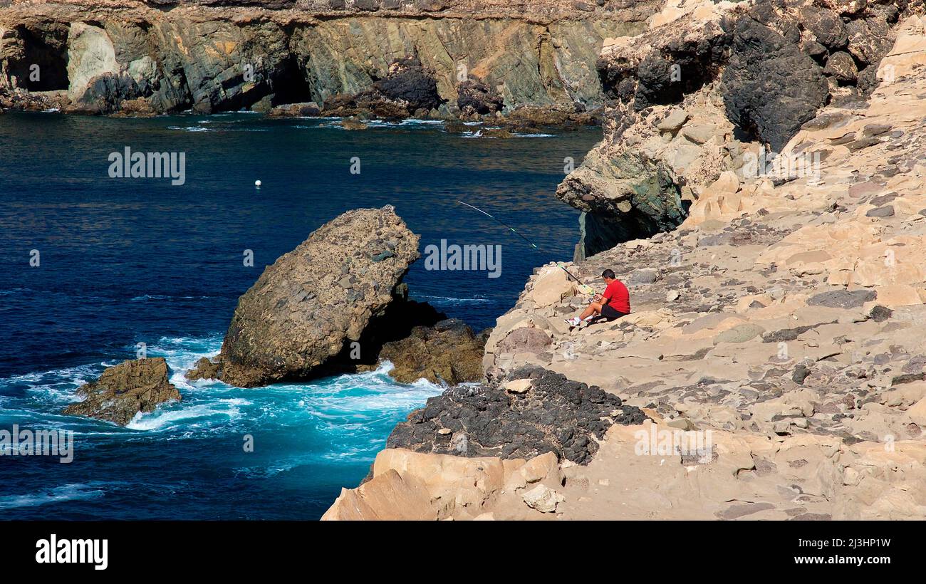 Spain, Canary Islands, Fuerteventura, west coast, Ajuy, single person sitting on rocks and looking at the sea, rocks in the sea, surf Stock Photo