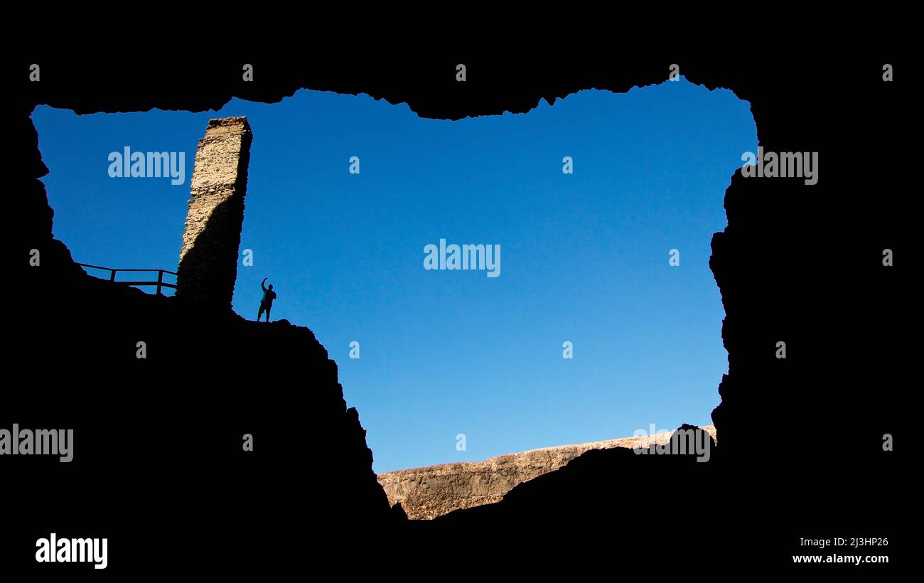 Spain, Canary Islands, Fuerteventura, west coast, cave, view from cave interior back to cave entrance, tower, single person silhouette, blue sky Stock Photo