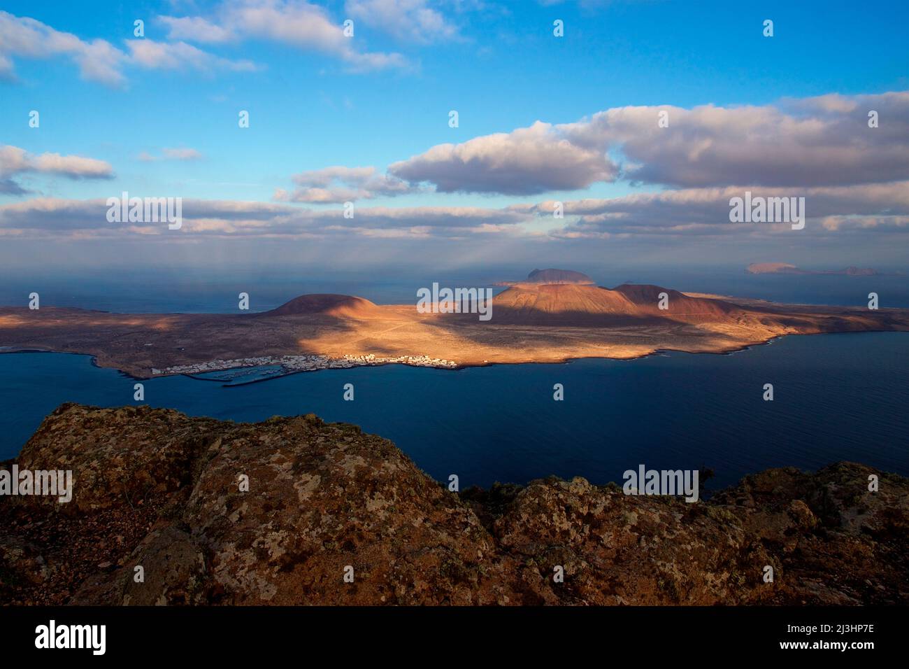 Canary Islands, Lanzarote, volcanic island, north of the island, after-thunderstorm mood, morning light, viewpoint, Mirador del Rio, created by Cesar Manrique, island La Graciosa, in the shade lying cliff of the Mirador in the foreground, La Graciosa partly in the morning light, sky blue and clear, clouds gray-white Stock Photo