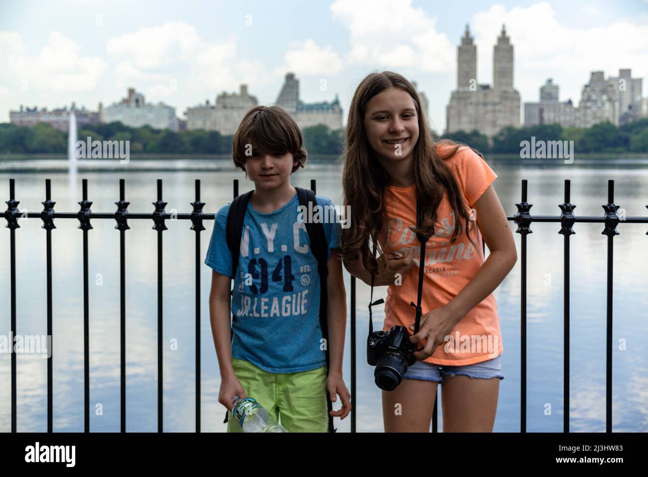 Central Park West, historic district, New York City, NY, USA, Young Boy and Girl next to the biggest Lake in Central Park, called Jacqueline Kennedy Onassis Reservoir. San Remo Building in the background 14 years old caucasian teenager girl and 12 years old caucasian teenager boy - both with brown hair and summer styling Stock Photo