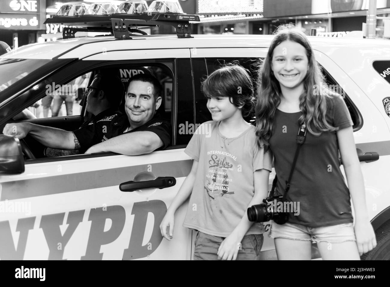 TIMES SQ - 42 Street, New York City, NY, USA, 14 years old caucasian teenager girl and 12 years old caucasian teenager boy - both with brown hair and summer styling posing with a police officer at times square Stock Photo