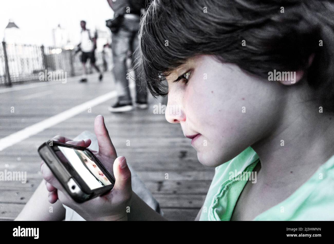 Brooklyn Heights, New York City, NY, USA, 12 years old caucasian teenager boy - with brown hair and in summer outfit starring at his mobile on Brooklyn Bridge over East River Stock Photo