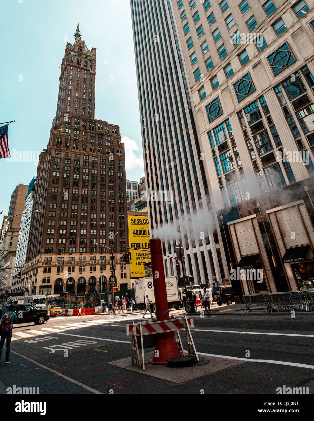 5 AV/W 58 ST, New York City, NY, USA, The typical New York City street view. Busy life, people, stores, American flags, cars and a steam vent in the middle of the street. Stock Photo